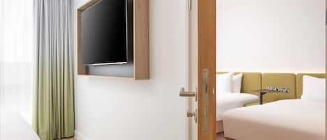 A hotel room with a bed, a TV mounted on the wall, a small table, and a window with curtains.