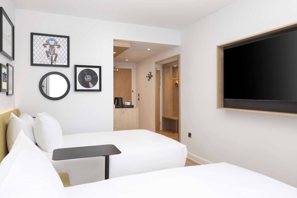 A modern hotel room with a bed, a small table, a TV, and a wardrobe.