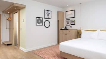 Quarto de hotel moderno com uma cama grande, um guarda-roupa de madeira, uma pequena escrivaninha e uma parede com quadros.