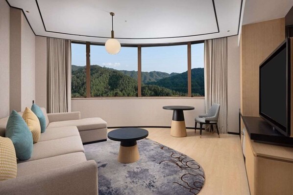 A modern hotel room with a large window offering a mountain view, a sofa, a round coffee table, and a flat-screen TV. - Hilton Garden Inn Jingdezhen Taoyuan Valley (Jingdezhen)