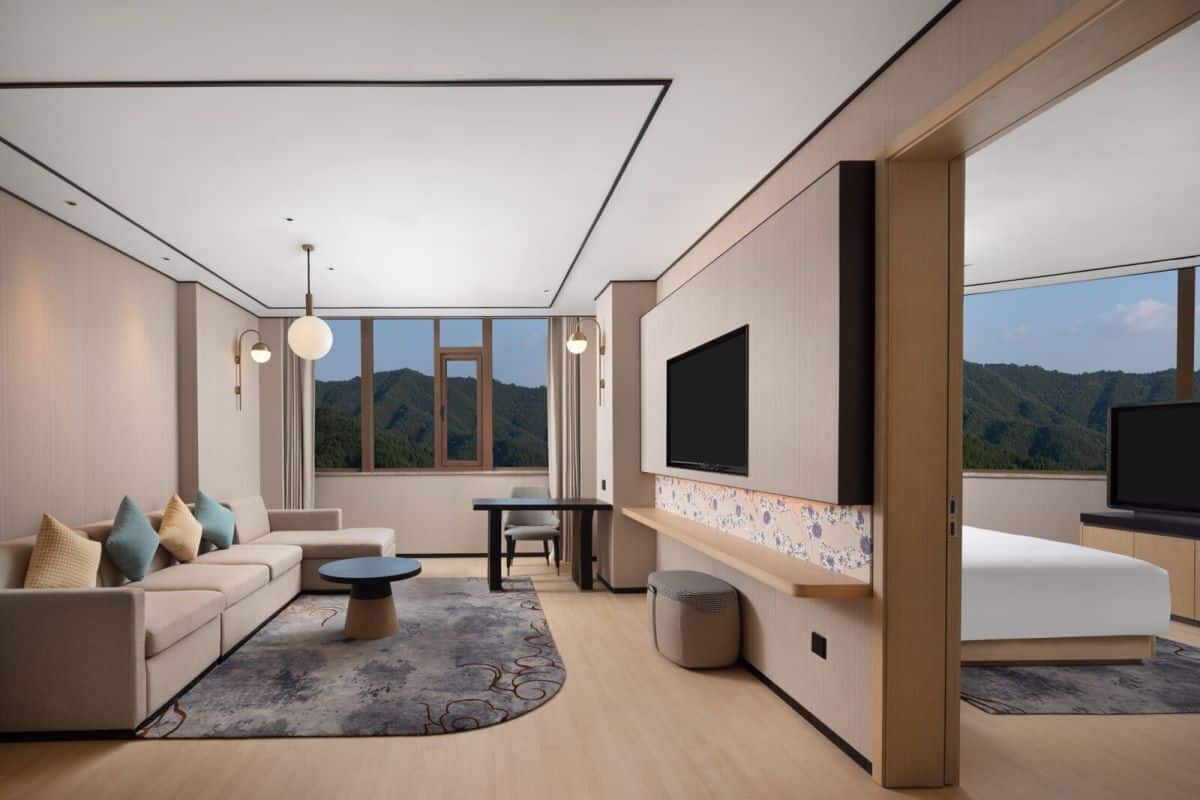 Un salon moderne avec un canapé, une table basse et un téléviseur, de grandes fenêtres offrant une vue sur les montagnes et un design minimaliste.