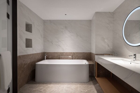 A modern bathroom with a large bathtub, a vanity with a mirror, and marble walls.
