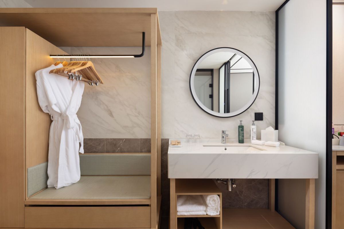 A modern bathroom with a wooden bench, a round mirror, a white sink, and neatly folded towels.