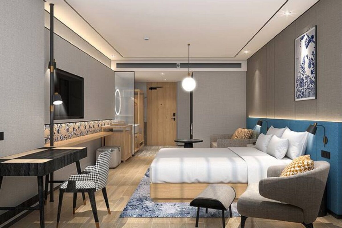 Ein modernes Hotelzimmer mit einem großen Bett, einem Schreibtisch, einem Sessel und einer Couch. An der Wand hängt ein Fernseher und über dem Bett hängt ein Bild.