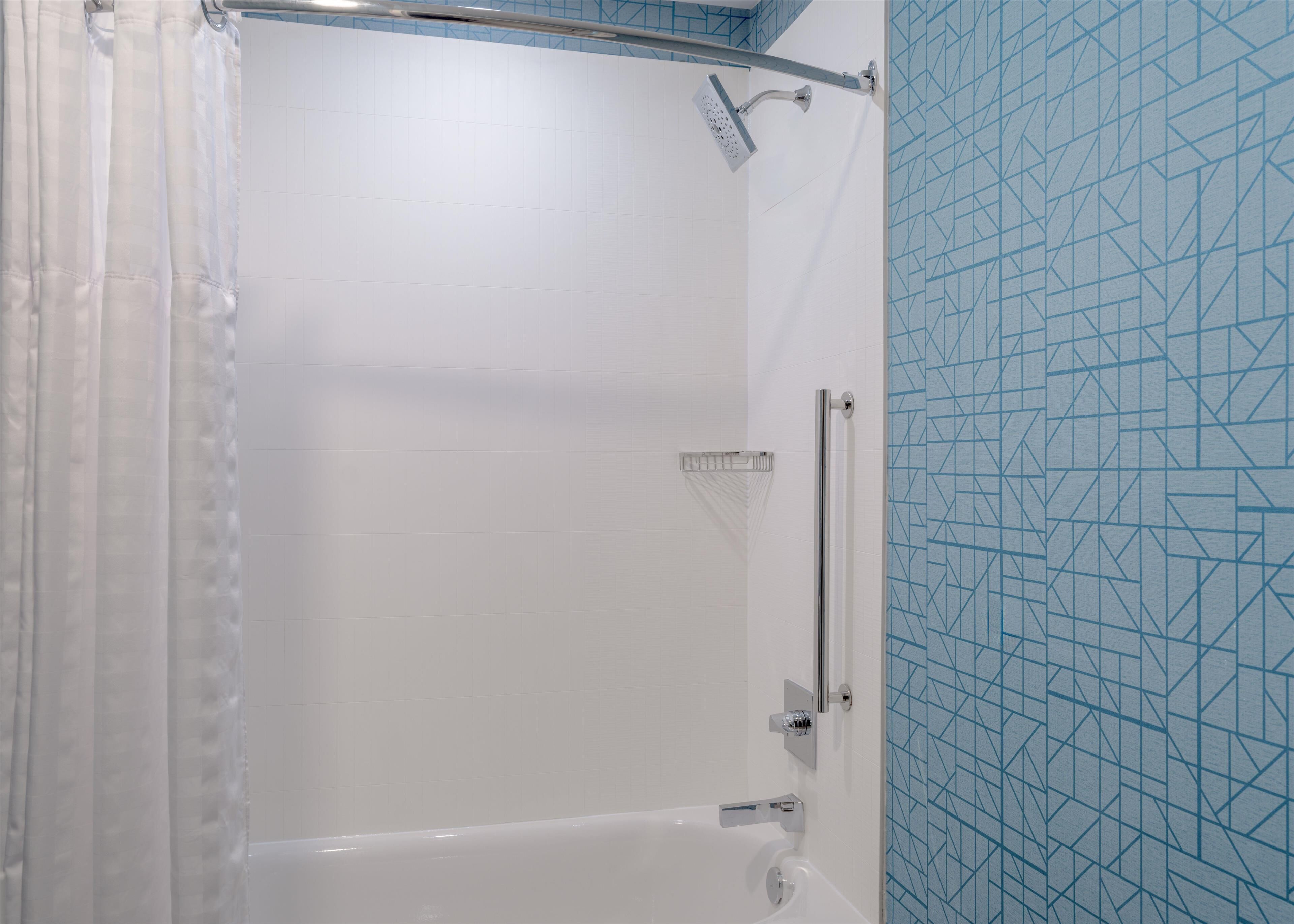 Ducha con puerta de vidrio, cabezal de ducha de mano y toallero en la pared.