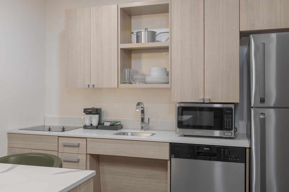 Une cuisine moderne avec des meubles de couleur bois clair, un réfrigérateur en acier inoxydable, un four à micro-ondes encastré et une machine à café.