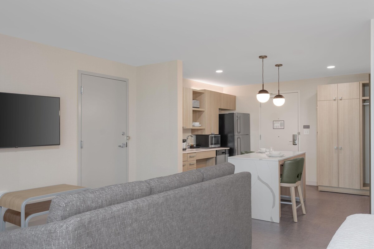 Un espace de vie moderne et compact, comprenant un coin cuisine, un canapé, un coin repas et un téléviseur fixé au mur.
