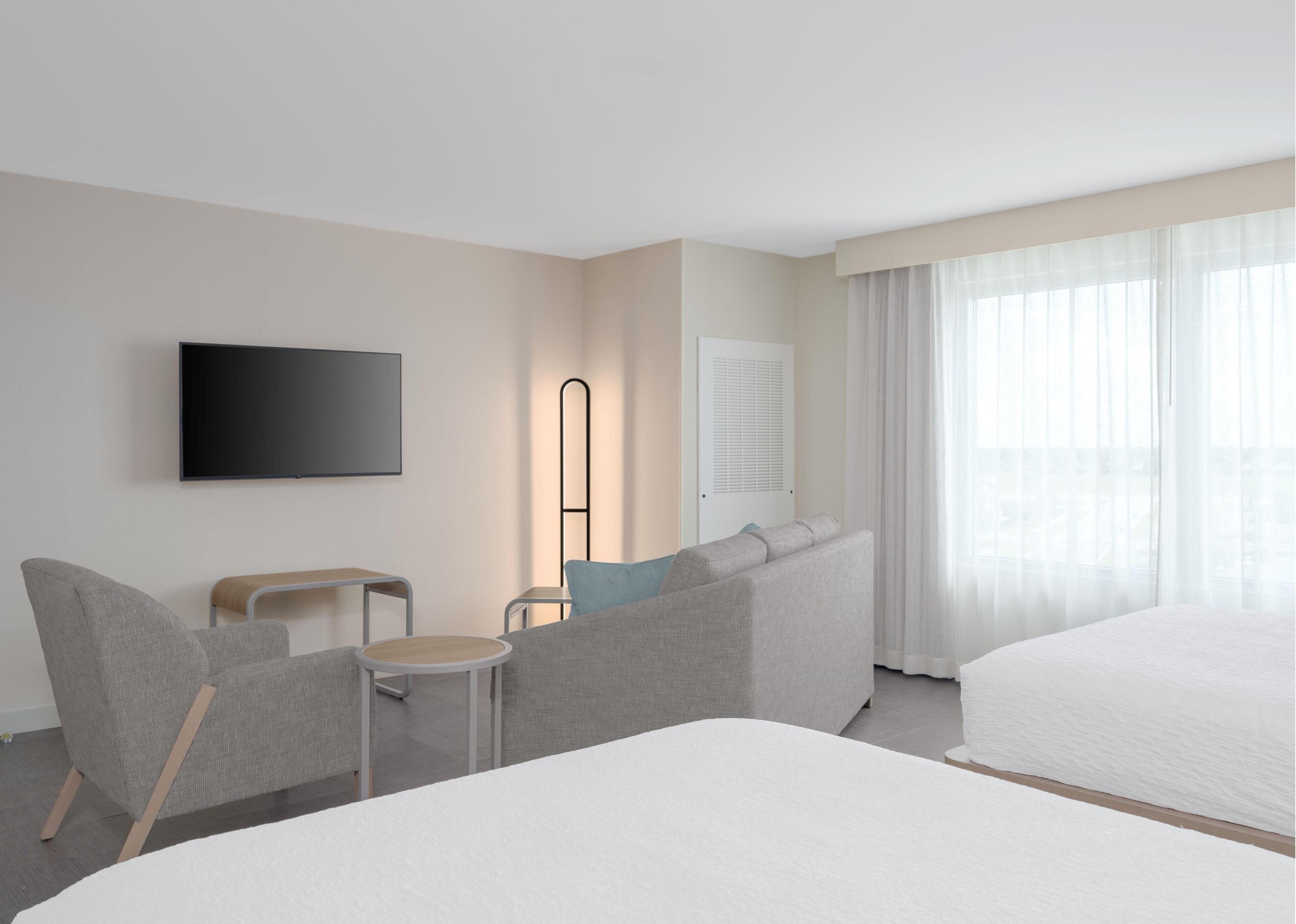 A hotel room with a large bed, a sofa, a chair, a TV, and a window with curtains.