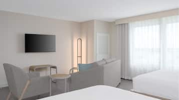 A hotel room with a large bed, a sofa, a chair, a TV, and a window with curtains.