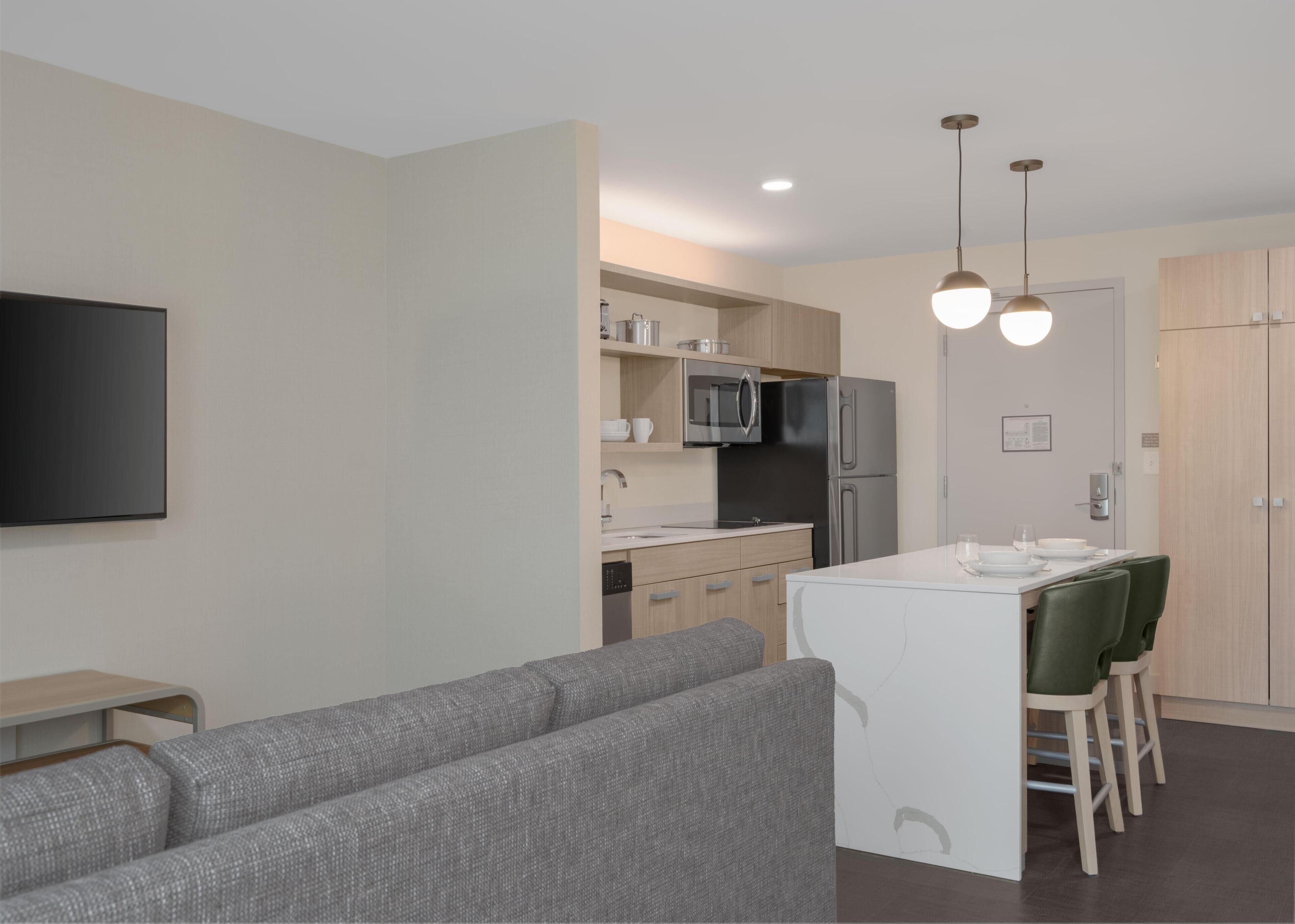 A modern kitchen with a built-in microwave, refrigerator, and dishwasher. There is a dining area with a white table and green chairs.