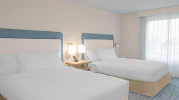 A hotel room with two beds, a nightstand with a lamp, and a window with sheer curtains.