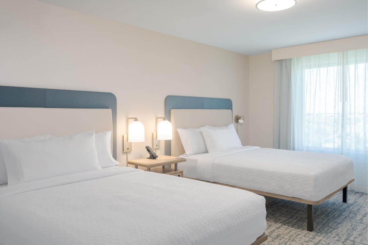 Una habitación de hotel con dos camas, cada una con cabecero, mesitas de noche y lámparas.