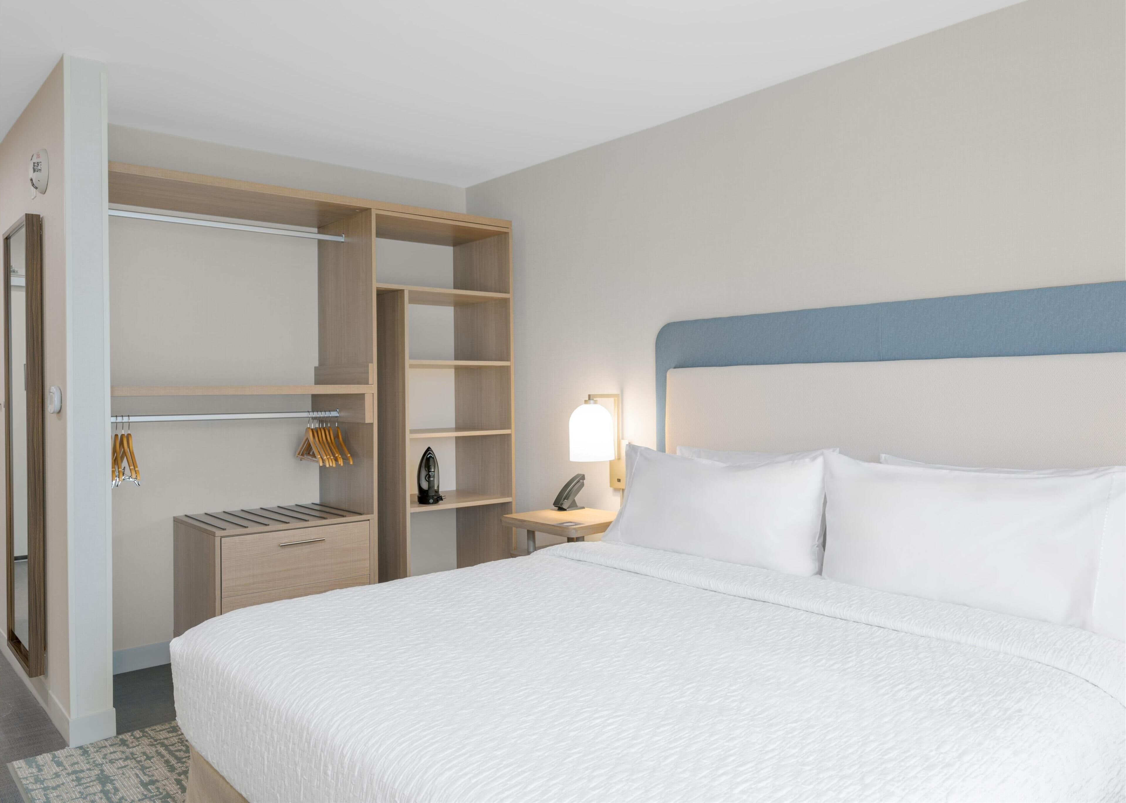 A hotel room with a large bed, a walk-in closet, and a bedside table with a lamp.