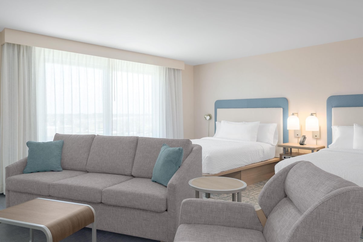 Habitación de hotel con sofá, dos camas individuales, una mesita pequeña y una mesita de noche con lámparas.