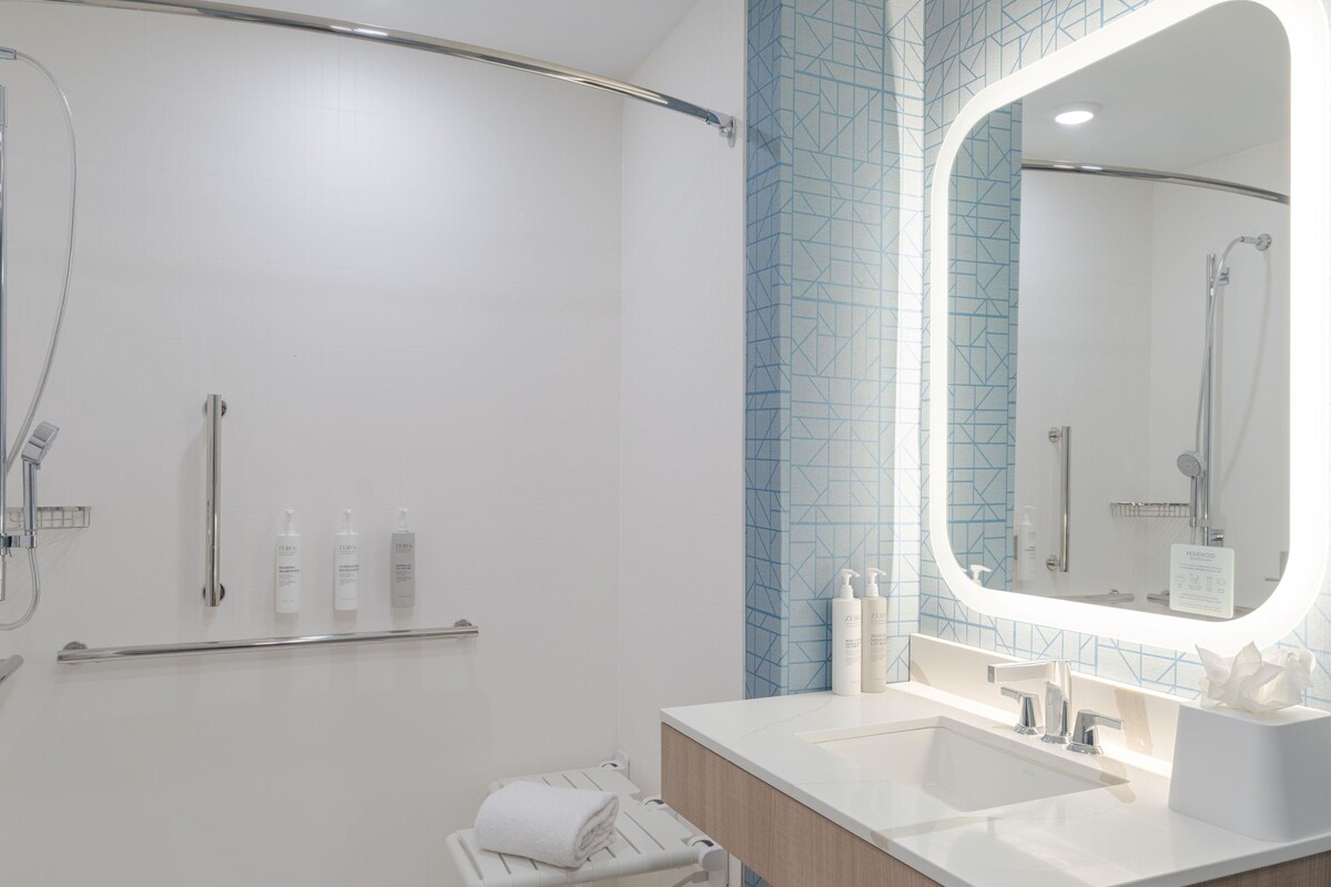 A modern bathroom with a walk-in shower, a vanity with a mirror, and toiletries on the wall.