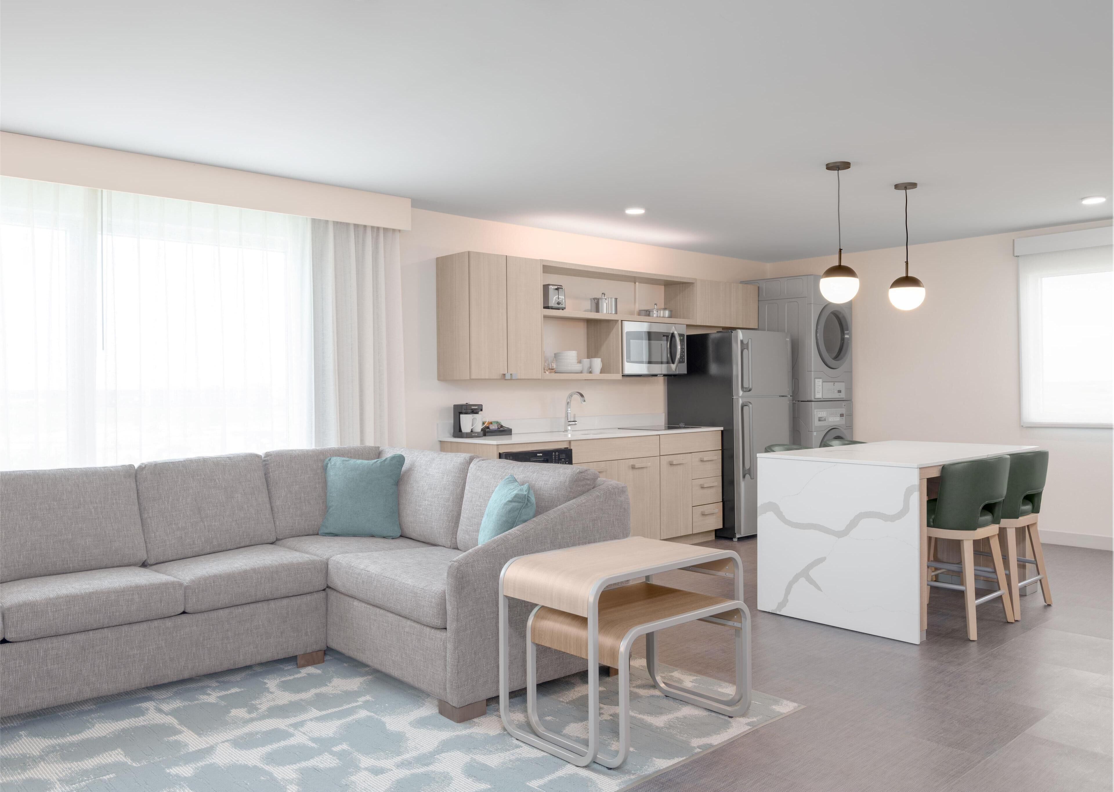 A modern kitchen with a grey sofa, a small dining table, and a built-in fridge.