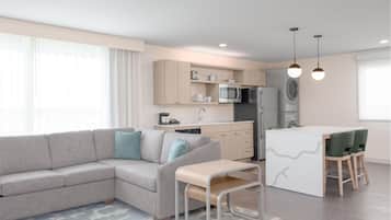 A modern kitchen with a grey sofa, a small dining table, and a built-in fridge.