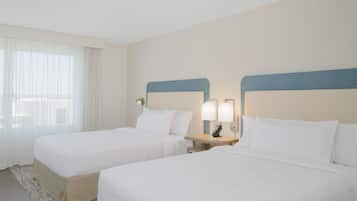 Una habitación de hotel con dos camas, una mesita de noche con lámpara y una ventana con cortinas traslúcidas.