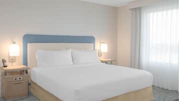 Una habitación de hotel con una cama grande, dos mesitas de noche y un ventanal con cortinas traslúcidas.