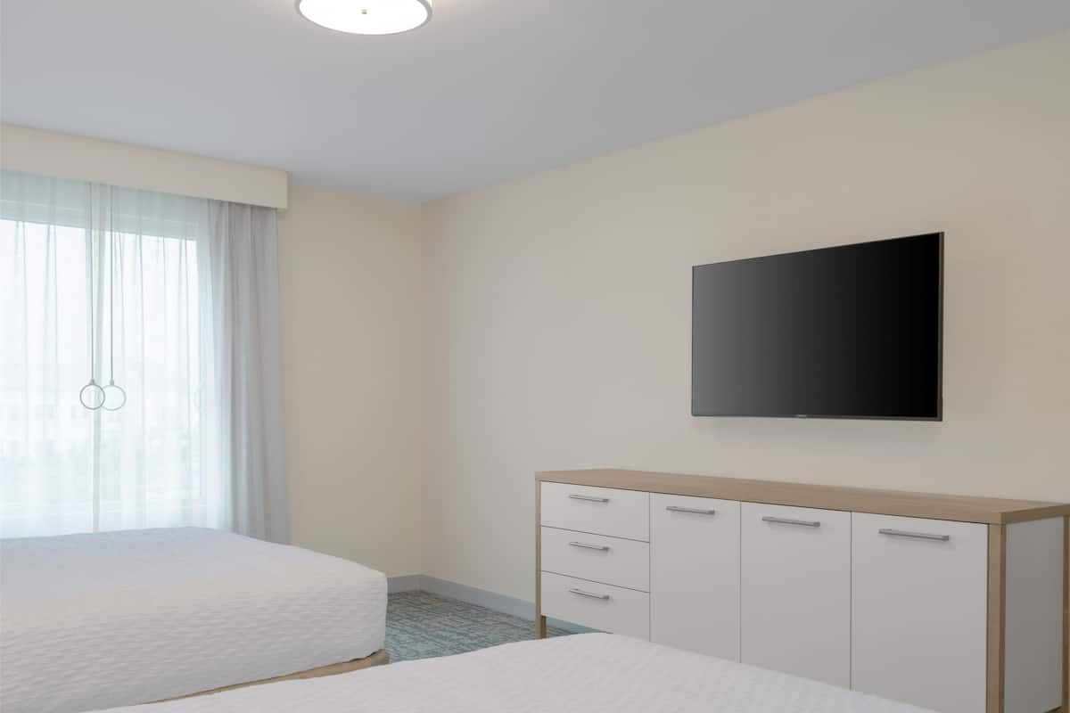 Habitación de hotel con dos camas, un televisor de pantalla plana montado en la pared y un mueble de madera con cajones.