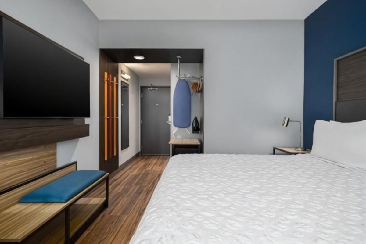 Une chambre d’hôtel avec un lit, un banc, une télévision, une armoire et un miroir.