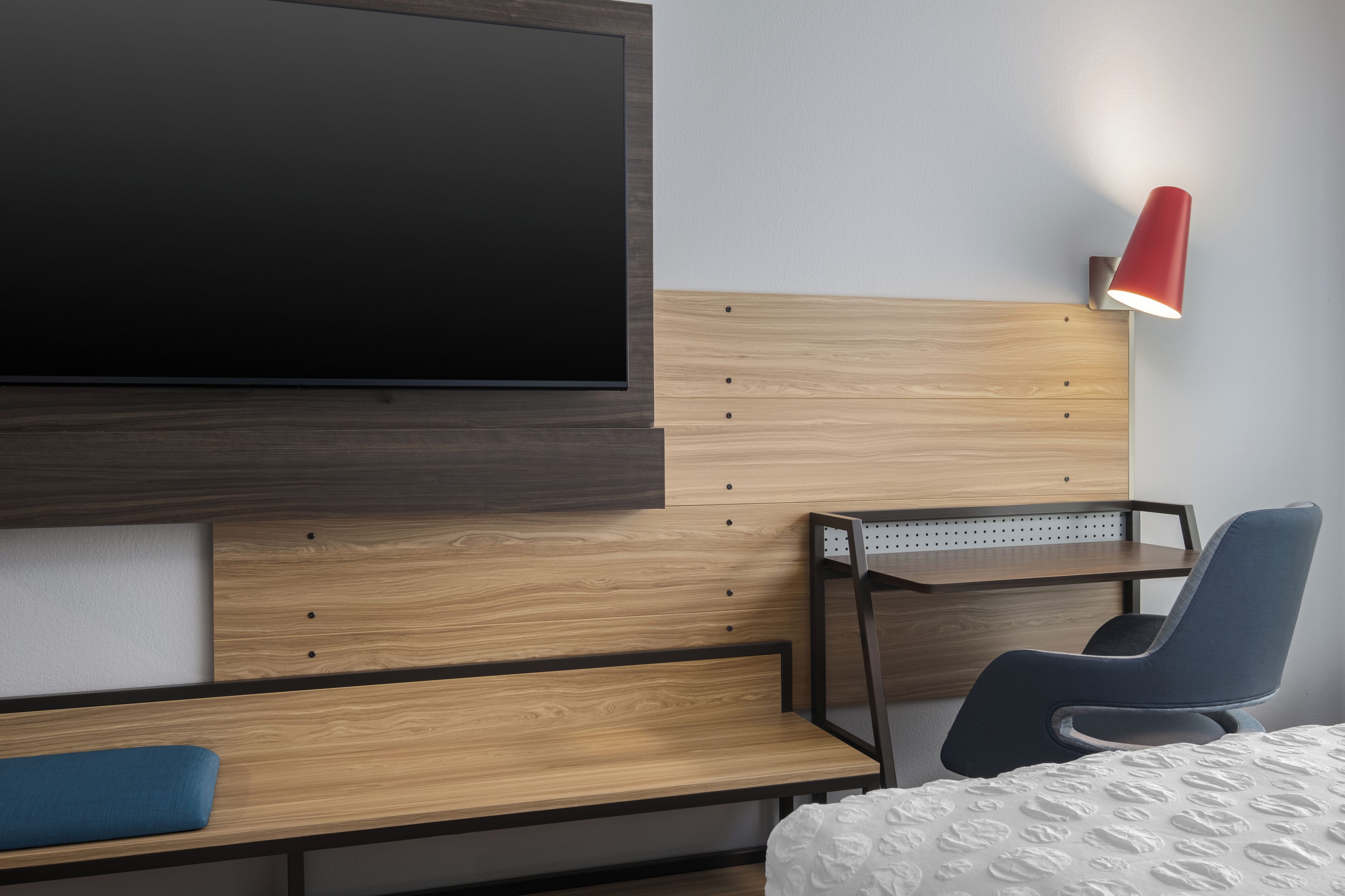 A modern hotel room with a flat-screen TV, a desk with a chair, and a bedside table.