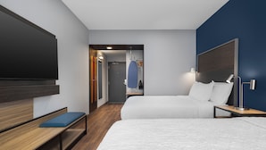 Una habitación de hotel moderna con una cama grande, una banca, un televisor, un escritorio y un vestidor.