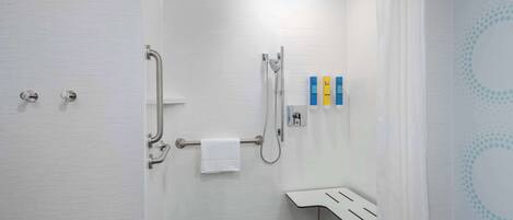 Un baño moderno con cabina de ducha, barras de apoyo, toallero y un lavabo pequeño con espejo.