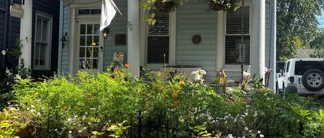 Una casa de dues plantes amb un porxo, un camí de maons i cistelles florals penjades.