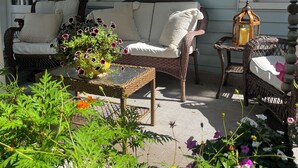 Een veranda met rieten meubels, een tafel met glazen blad en potplanten.