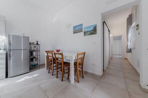 Una cocina con un refrigerador blanco, sillas de madera, una mesa blanca y dos cuadros colgados en la pared.