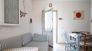 A living room with a striped sofa, a dining table with chairs, and a window with curtains. - Villetta Diana Marina by Rentbeat (Ostuni)