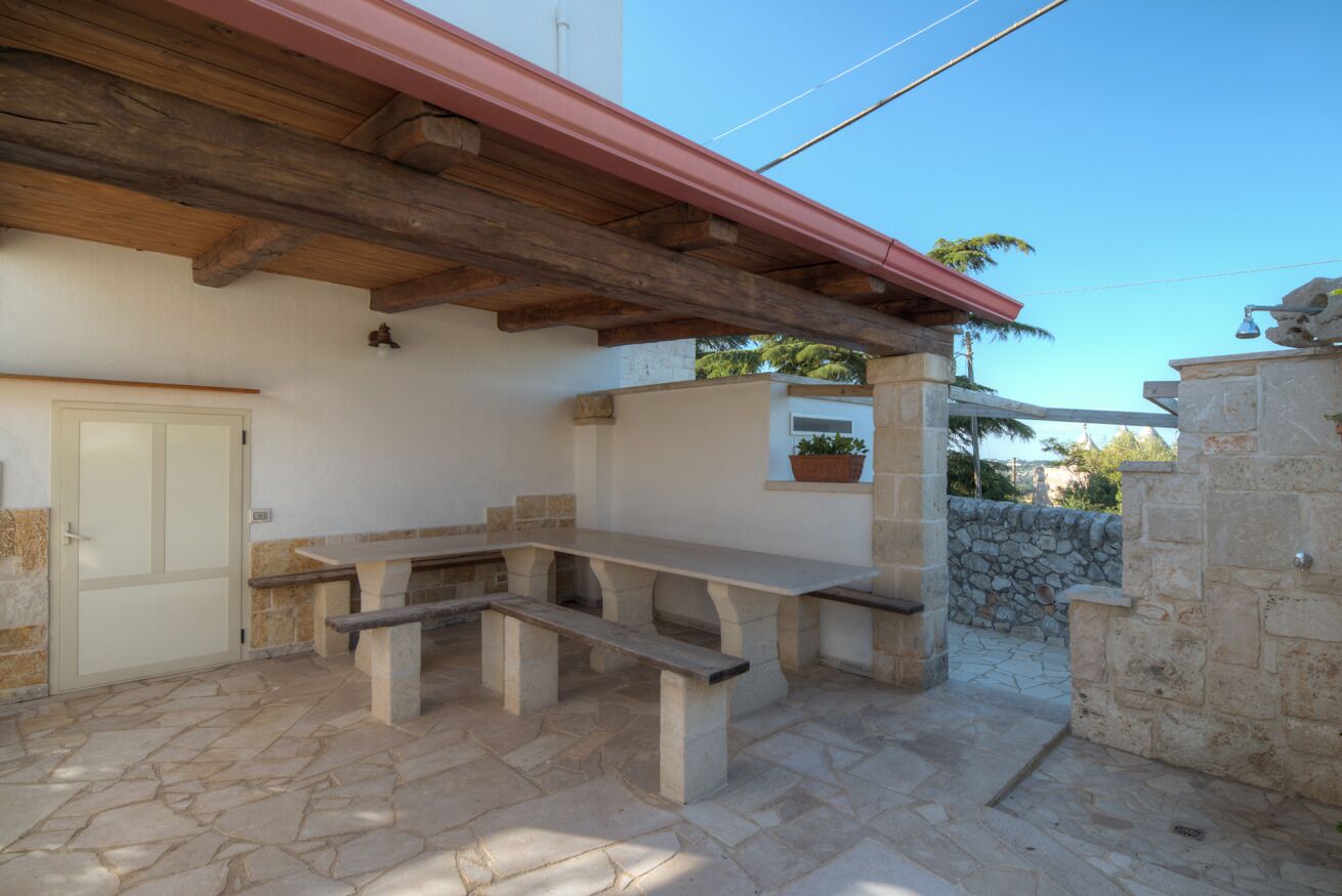 An outdoor patio with stone flooring, a wooden pergola, a stone bench, and a white door.