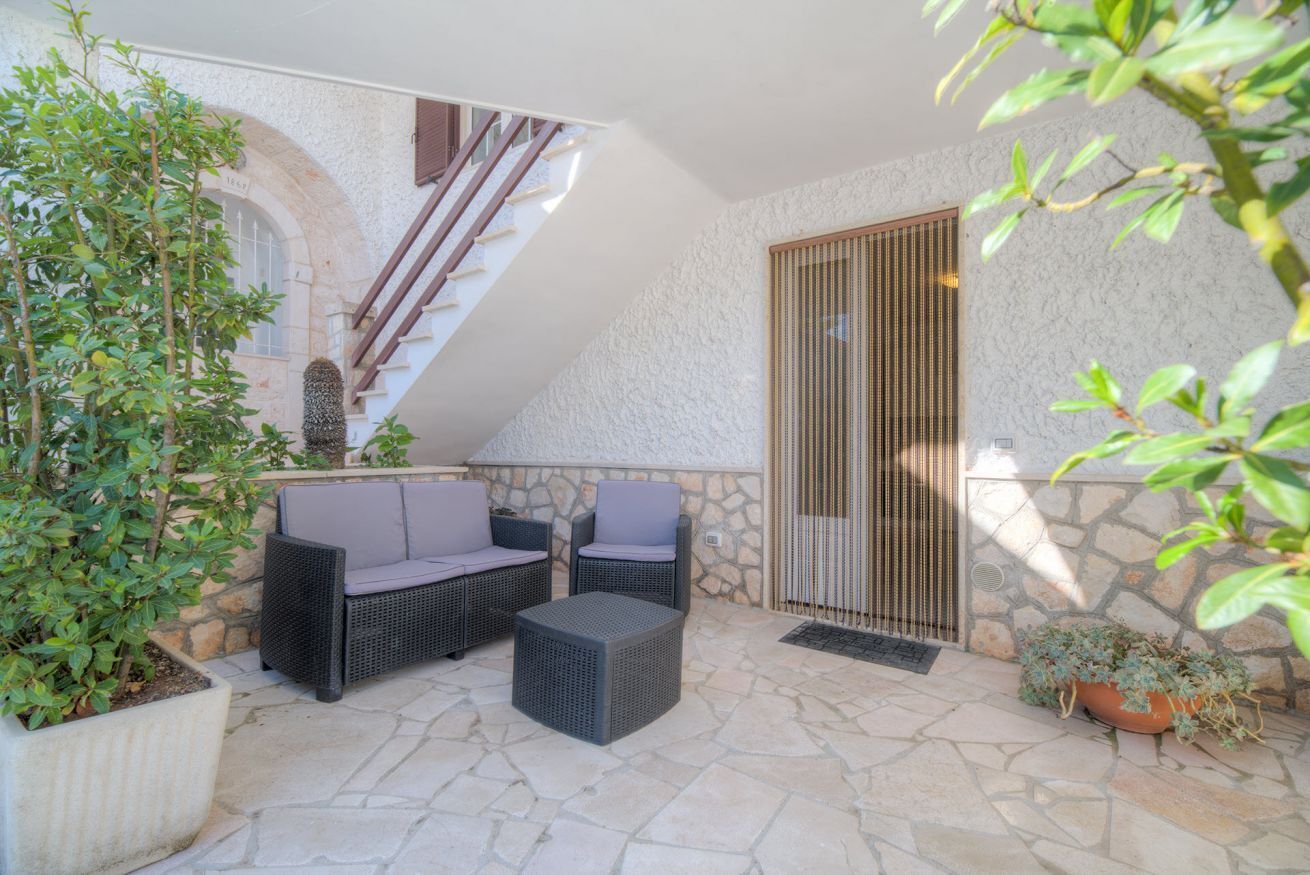 Un patio al aire libre con mobiliario de mimbre, paredes de piedra y una escalera.