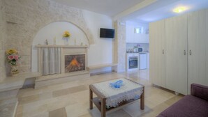 A living room with a fireplace, a television, a kitchen in the background, and a sofa. - Trullo Rosmarino by Rentbeat (Locorotondo)