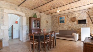 A rustic stone-walled room with a dining table, chairs, a sofa, and a television. - Zi Nunzie by Rentbeat (Abbateggio)