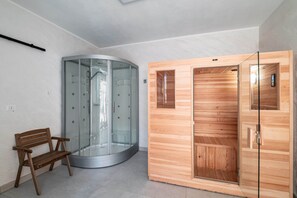 Une salle de bain moderne avec une douche à parois de verre, un sauna en bois et un banc.