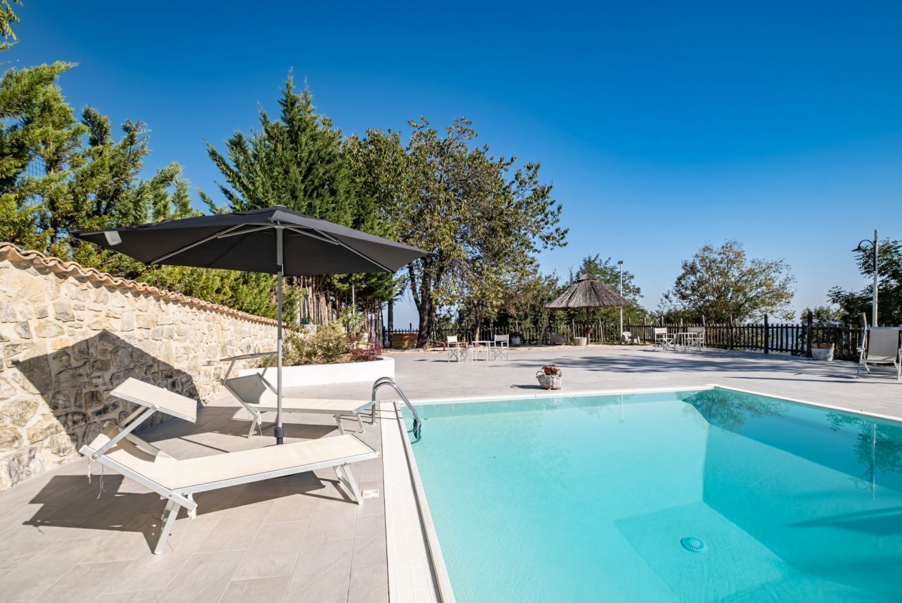 A swimming pool with lounge chairs and umbrellas, surrounded by stone walls and trees.