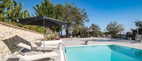 A swimming pool with lounge chairs and umbrellas, surrounded by stone walls and trees.