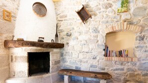 A stone fireplace with a bench, a shelf with books, and a wall-mounted wooden tray. - Zi Pasquale by Rentbeat (Abbateggio)