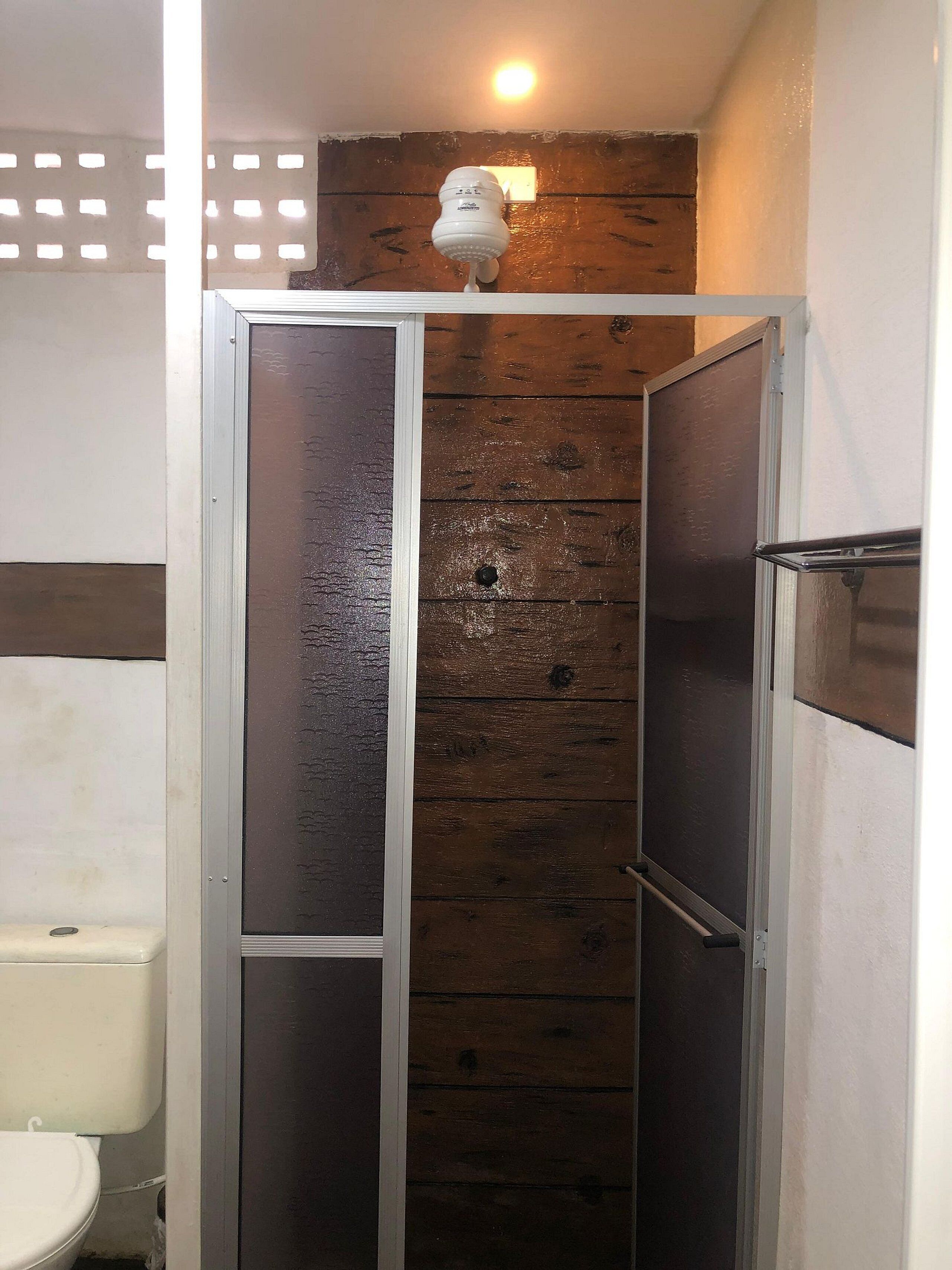 A bathroom with a wooden panel wall, a white toilet, and a shower enclosure.