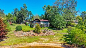 A lakeside cabin with a deck, surrounded by lush greenery and trees.