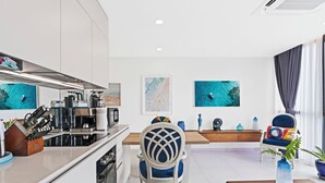 A modern kitchen with a dining area, featuring a white and blue color scheme, a coffee machine, and a view of the ocean through large windows. - A133 -  Top Floor Lagoon View (Sint Maarten)