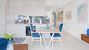 A modern kitchen with white cabinets, a dining area with blue chairs, and a large clock on the wall. - A133 -  Top Floor Lagoon View (Sint Maarten)