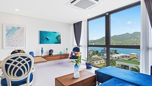 A modern living room with a large window, a blue sofa, a white chair, and a coffee table. - A133 -  Top Floor Lagoon View (Sint Maarten)