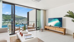 Una sala de estar moderna con un televisor grande, un sofá, una mesita de centro y vistas a un puerto y montañas.