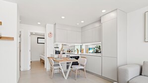 Una cocina moderna con armarios blancos, un comedor con dos sillas y un sofá en la sala.