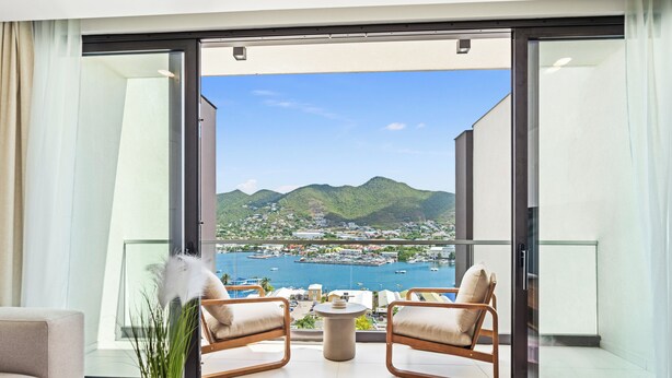 Una sala de estar moderna con un amplio ventanal corredero que da a un balcón con vistas a un pueblo costero y montañas.