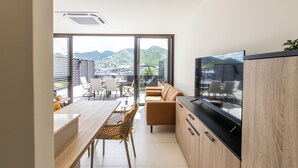 A modern kitchen with a large TV, wooden cabinets, and a dining area with a view of mountains. - A105 - Breathtaking Apartment with Garden (Sint Maarten)