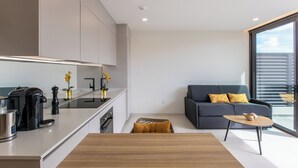 A modern kitchen with a coffee maker, a stove, and a sink. There is a sofa with yellow pillows and a small table with a bowl. - A105 - Breathtaking Apartment with Garden (Sint Maarten)